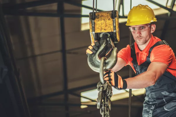  A construction worker using a piece of lifting equipment, an overhead crane in a construction warehouse. 