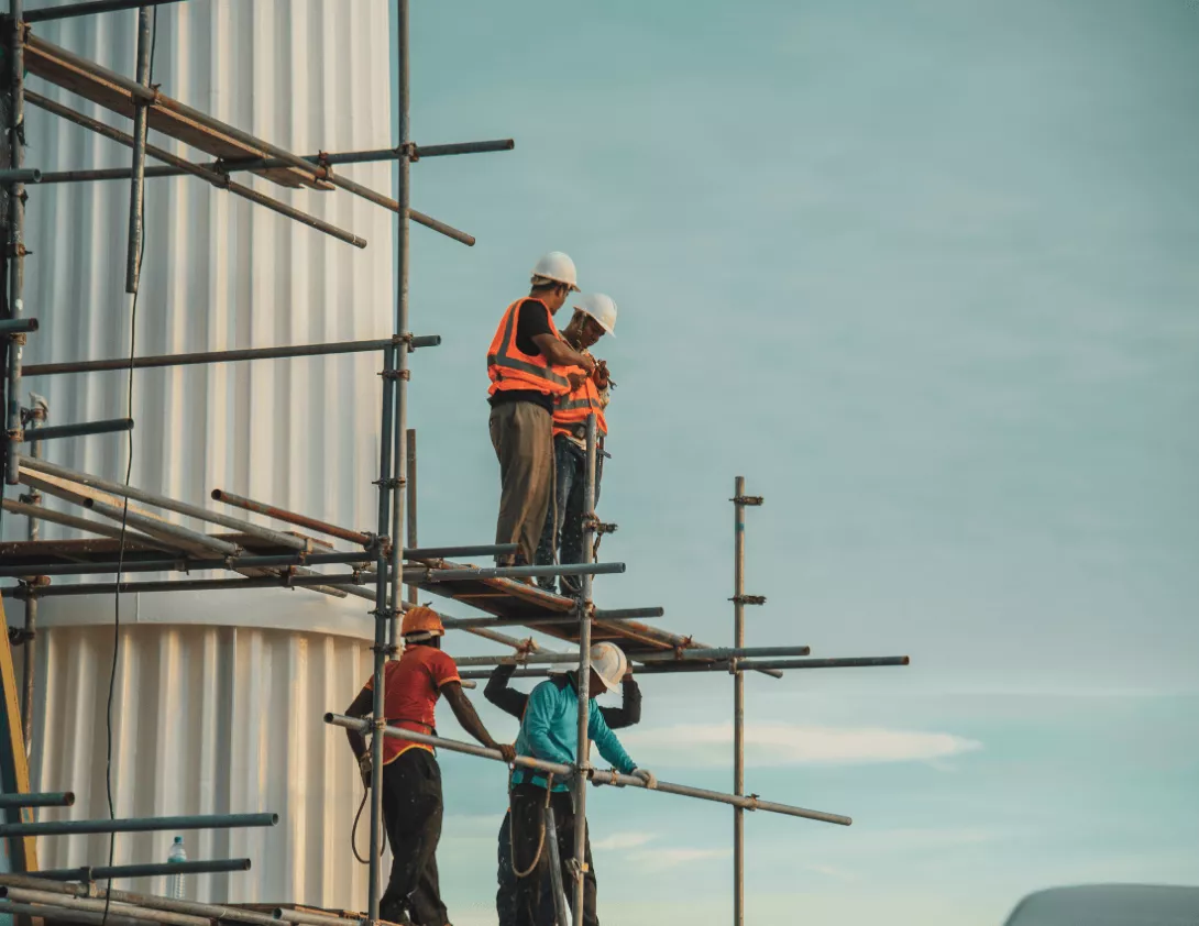 Construction workers in high visibility jackets on scaffolding working at a height discussing how to prevent workplace falls by using fall protection equipment.