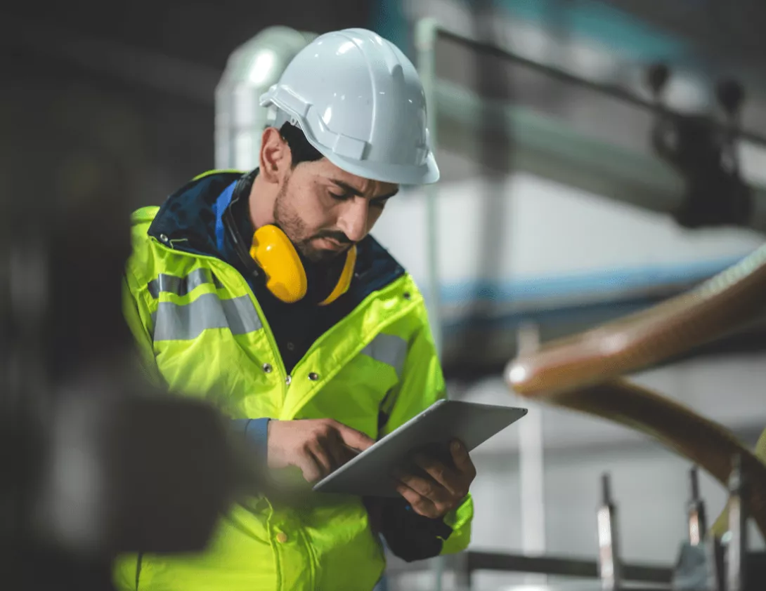 Construction worker looking at iPad considering the hierarchy of control when working from a height whilst wearing a hard hat and high visibility jacket.